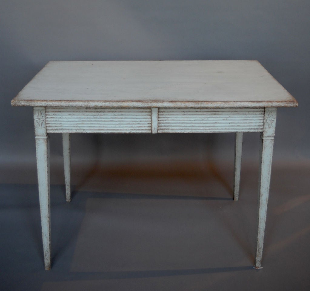 Period Gustavian table in pale blue-white paint, Sweden circa 1820, with two drawers with horizontal fluting. Square tapering legs below corner blocks with carved rosettes. Would also work nicely as a writing table.