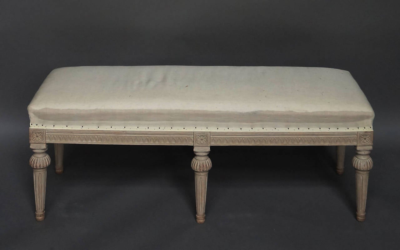 Wide bench in the Gustavian Style, Sweden, circa 1900. Lambs tongue molding on the apron and rosettes above the round tapering legs and simple turned feet. Upholstered seat.