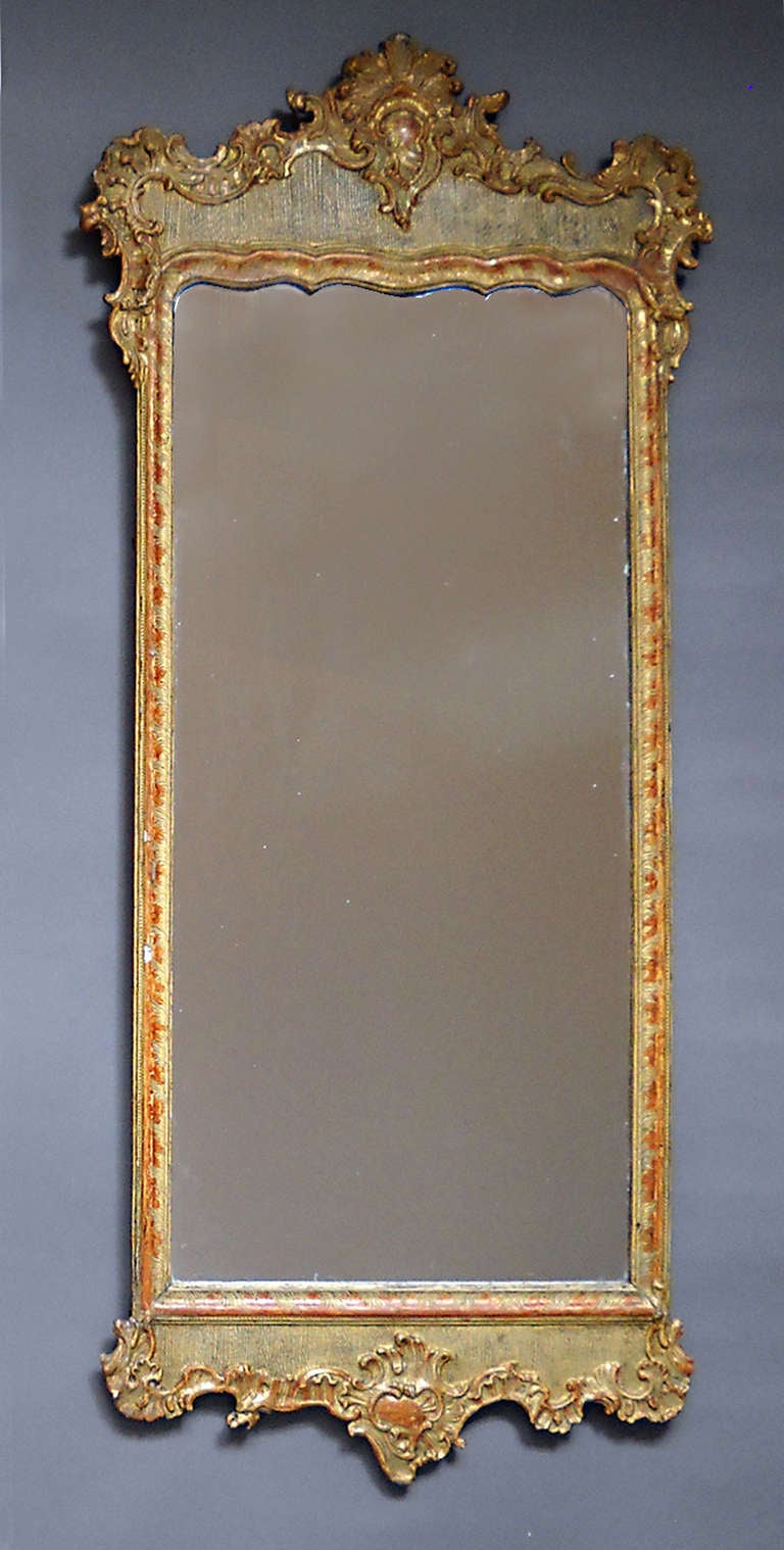 Period rococo mirror, Denmark circa 1770, with original surface, mirror glass and back. The mirror is surrounded with a simple frame with sgraffito detail and has a panel at top and bottom with rocaille carving around a crosshatched ground.