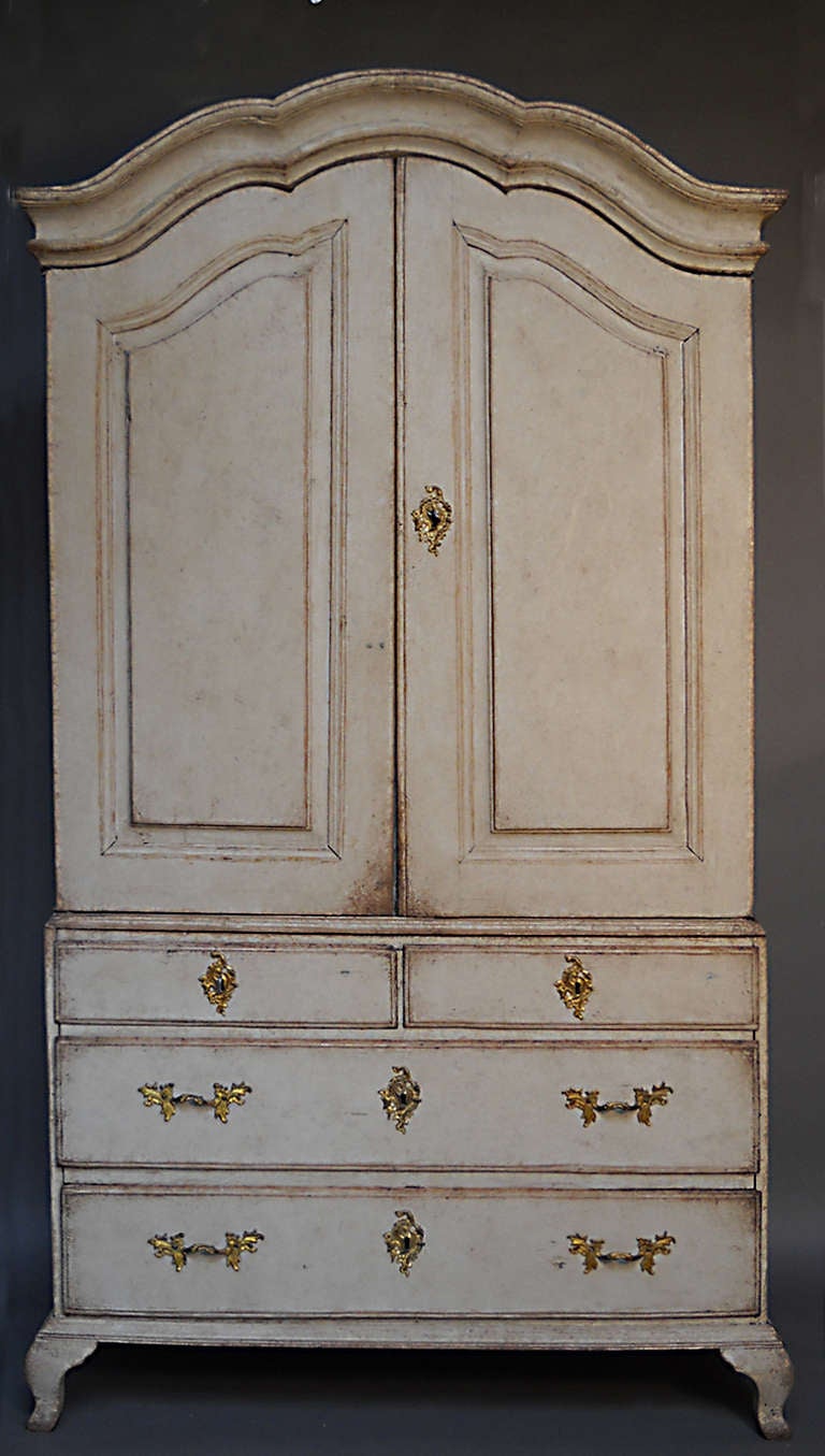 Period rococo cabinet in two parts, Sweden circa 1760. Upper section has two raised panel doors and arched cornice. The interior has two shelves and a spoon rack, as well as three small drawers.

The lower section has two small drawers over two