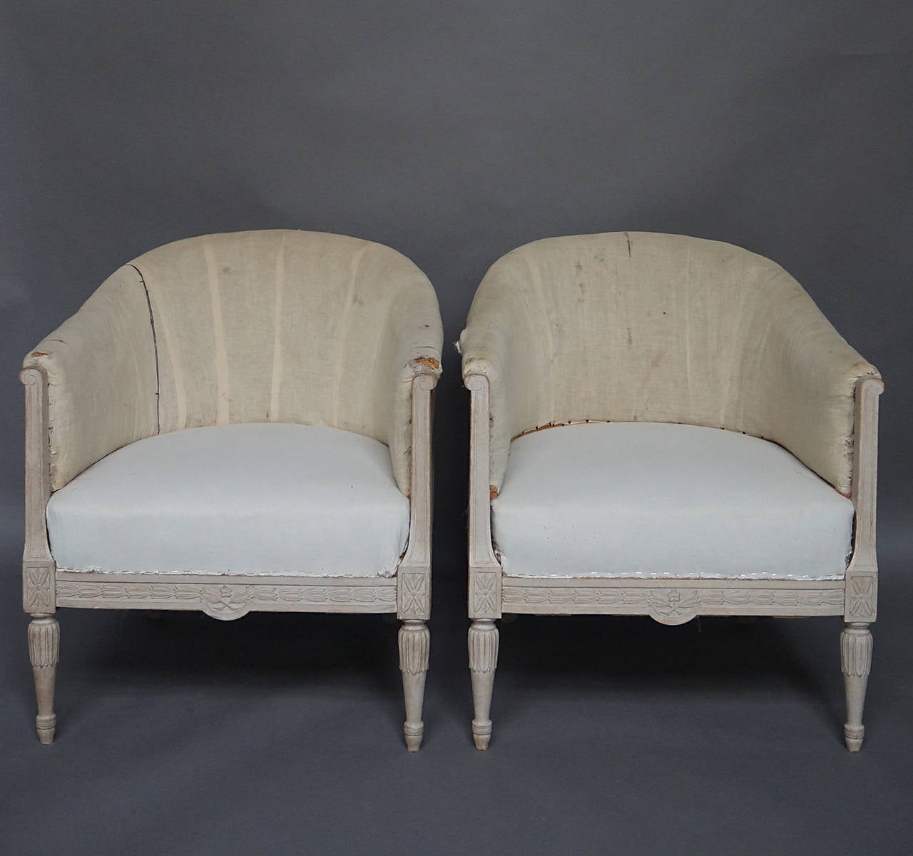 Pair of club chairs, Sweden, circa 1910, in the Gustavian Style. Carved frame with bell-flowers, rosettes, and lotus details. Upholstered seats and backs.