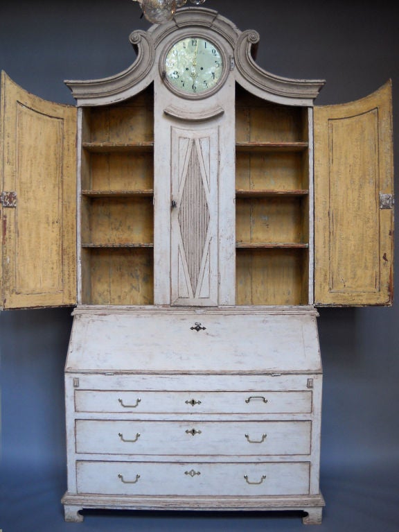 Swedish secretary, circa 1820, with a Mora clock in the upper section. Raised panel doors open on three shelves on either side of the clock's pendulum. In the lower section, there are three full-width drawers under the slanted front and multiple