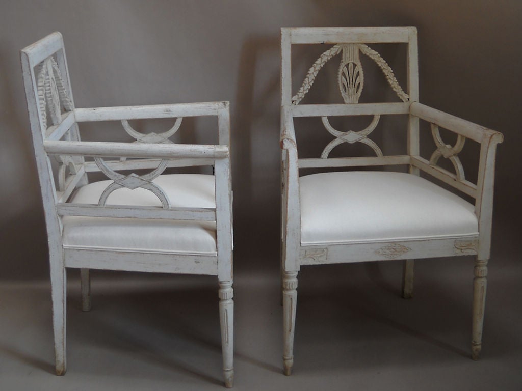 Pair of Swedish armchairs, circa 1910, in the Empire or Carl Johan style. The open backs show a central wheat sheaf with reeded column and a laurel swag on either side. Below that and also supporting the arms are curule-form brackets that reflect