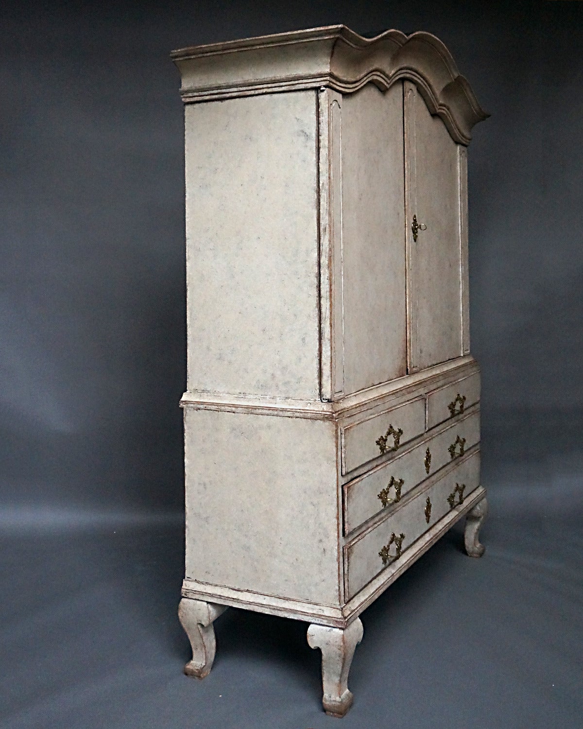 Two part Rococo cabinet, Sweden, circa 1760, with original hardware and interior painted surface. The top section has an arched cornice, carved pilasters and three interior shelves. The lower section has two small drawers over two full-width ones