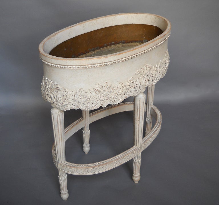 White painted oval jardinière, Sweden, circa 1900, with beaded detail on the apron above carved flowers and foliage. Tapering legs with lotus leaves connected by a carved stretcher. Original copper liner.