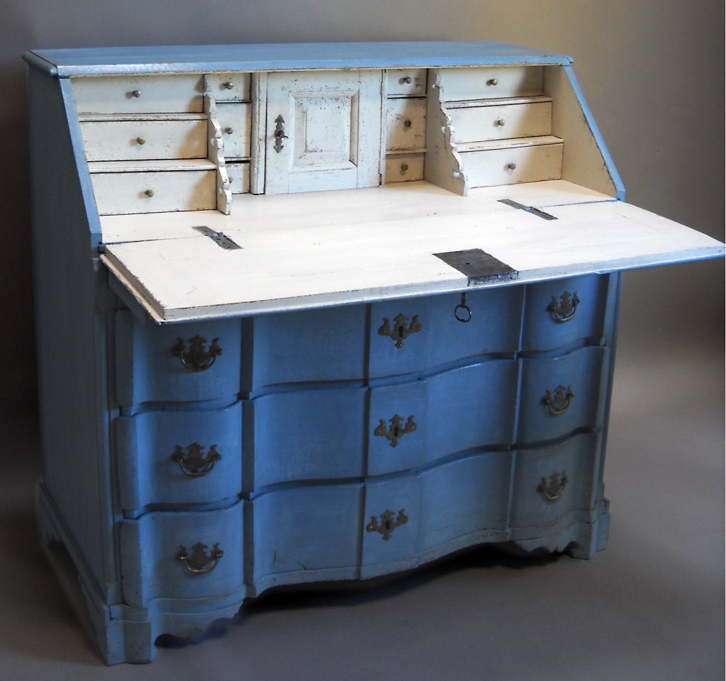 Swedish rococo writing desk, circa 1780, with bow front and three drawers below the slanted writing surface. The interior has four banks of drawers and a central compartment. Early brass hardware and secondary blue and white paint.