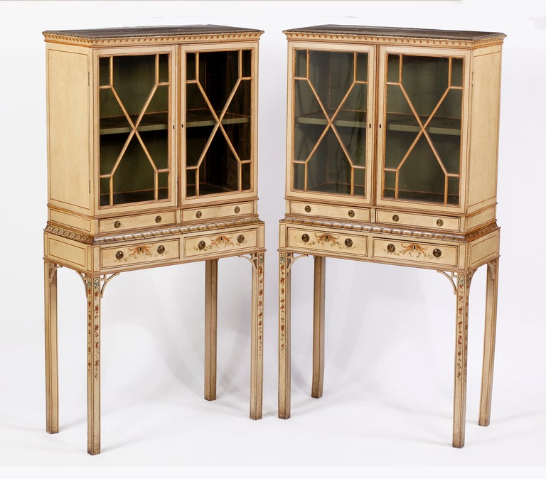 Each with a molded cornice above a pair of diamond mullioned glazed doors opening to a shelf, over two a pair of drawers, raised on square legs headed by pierced brackets, painted with ribbons, flowers and trading vines, two drawers bearing the