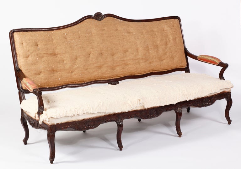 A Regence Carved
Stained Beechwood Canapé
18th Century

With a serpentine rocaille-carved crestrail, with winged sides and scrolling arm supports, with a similarly carved serpentine rocaille crestrail, on shell-headed cabriole legs ending in