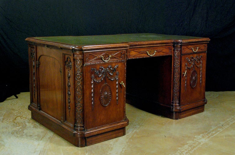 The shaped top with a tooled leather insert over two pedestals with fitted interiors, one side with shelves the other side with three drawers.  Each pedestal with carved details throughout, all resting on a shaped plinth base.

Provenance: