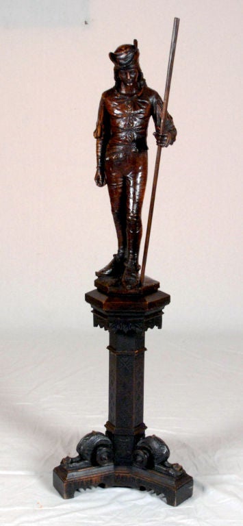 The figure is highly detailed on a pedestal with carved details throughout including three figural carvings on the tripod form base.