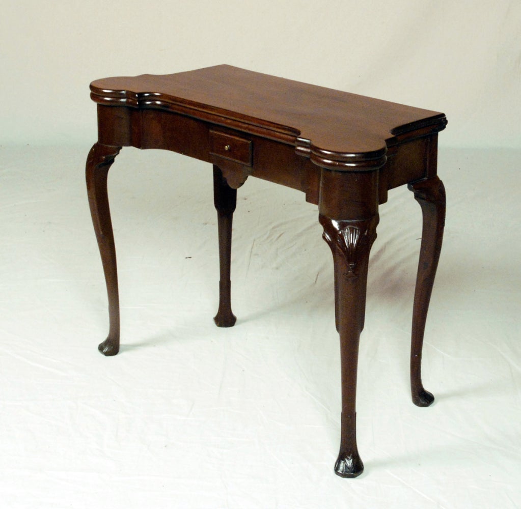 The oblong hinged top with outset rounded corners opening to a baize lined playing surface inset with counter wells, above a conforming frieze fitted with a small drawer, raised on shell carved cabriole legs ending in leaf carved pad feet