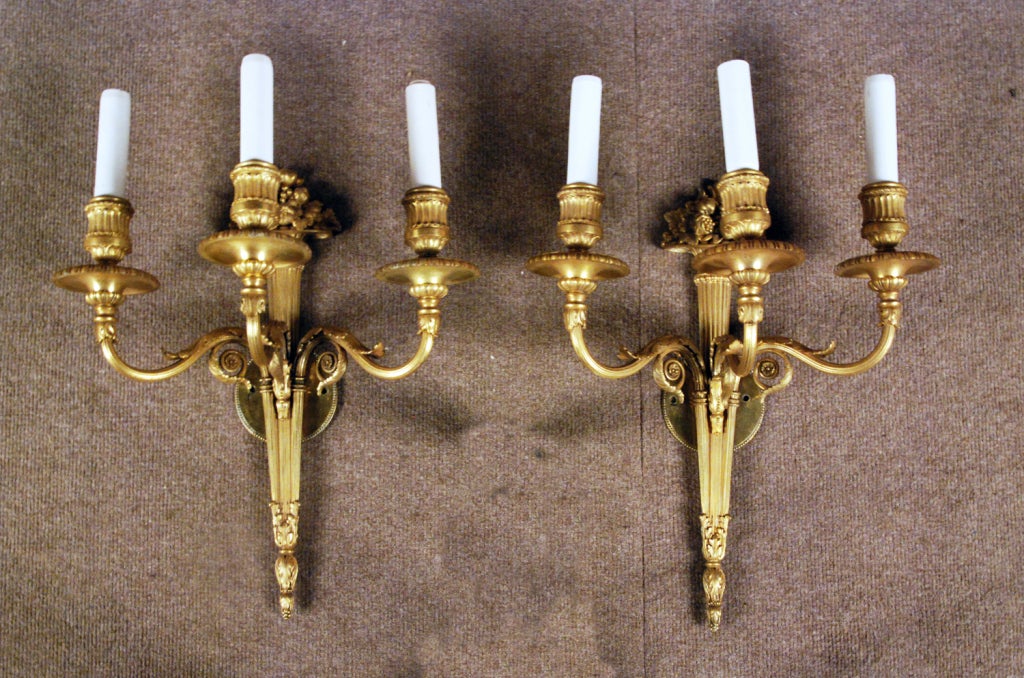 A Fine Pair of Louis Style Gilt Bronze 
Three Arm Sconces
By Caldwell & Co.
American, circa 1900-1910

Each back plate in the form of a flaming touch hung with drapery swags issuing a set of 3 scrolled foliate cast candle arms with leaf tip