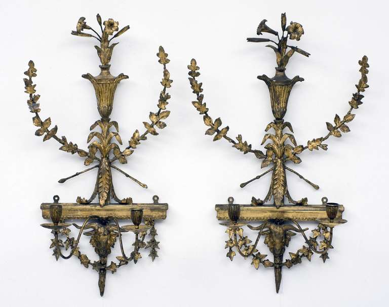 Pair of elegant Neoclassical Adam period carved, gessoed and gilded two-light wall sconces with lily-filled urn and crossed branches, the base with ivy vine and ram’s head.  Height: 24.25