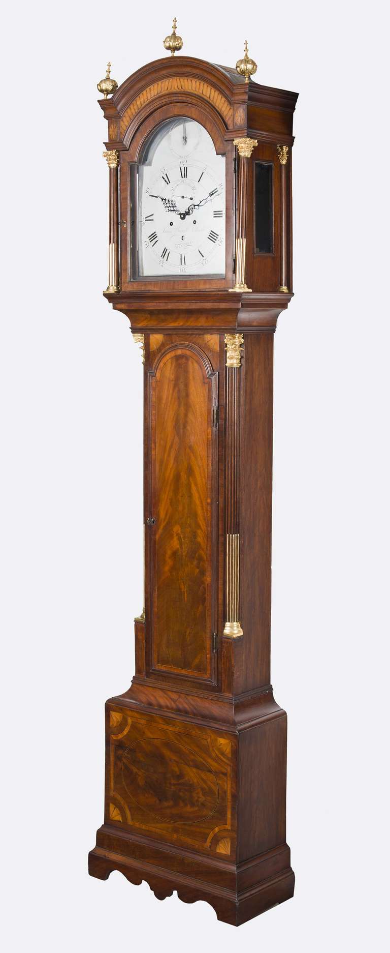 Georgian mahogany tall case clock by James Worrel Clarke, London. Satinwood inlaid arched hood with three gilded finials, detached fluted columns to hood with gilded Corinthian capitals, recessed quarter fluted columns to trunk with gilt inlay,