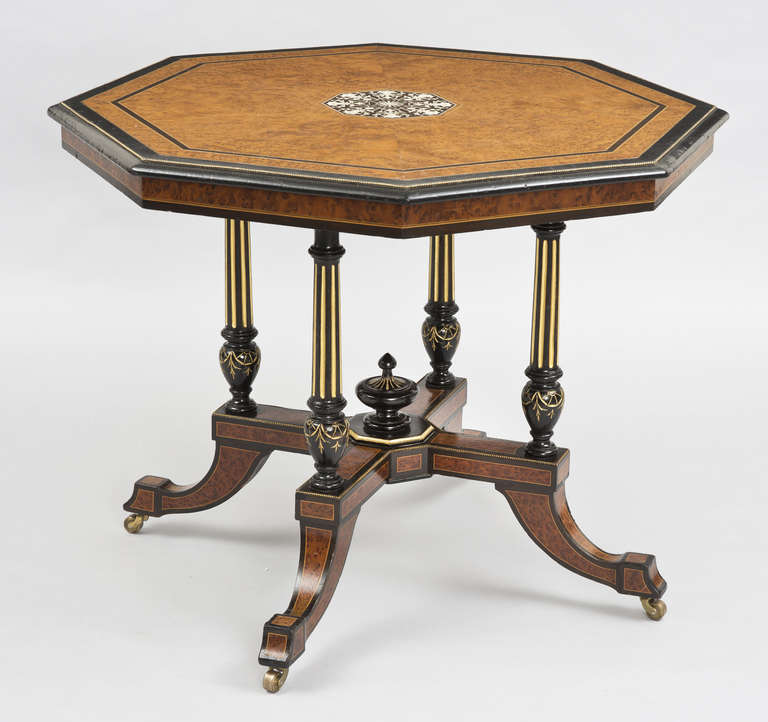 Burl elm and ebonized inlaid octagonal center table, the top with central medallion of eight pen work masks and scrollwork set within stringing, banding and brass beading, four gilt fluted supports joined by X-shaped platform with urn finial in
