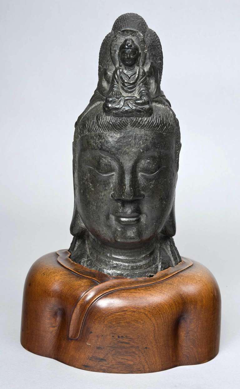 Stone bust of Bodhisattva with serenely carved features and elaborate coiled coiffure with carved Buddha headdress set into a later handmade carved wooden base. Possibly from Thailand.