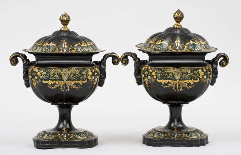 Pair of Regency ornately shaped black lacquered and parcel-gilt tole covered chestnut urns with scroll handles, the covers with brass acorn finials, decorated with sprays of gilded, ivory and red polychromed flowers and foliate patterns.  These urns
