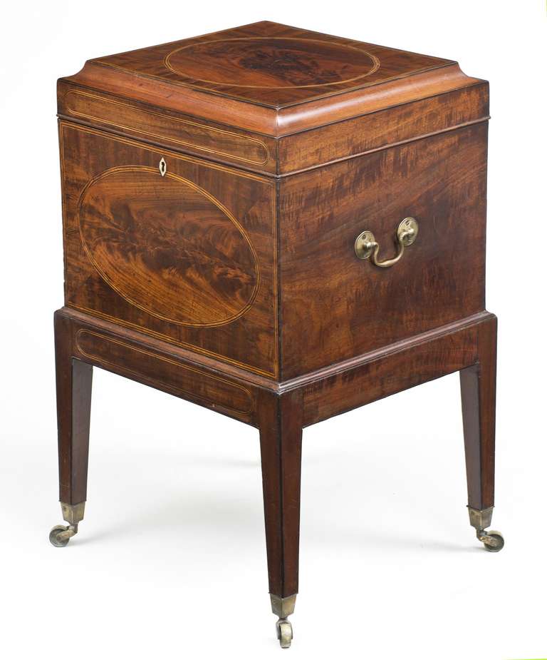 Sheraton mahogany and satinwood cellarette inlaid with round and oval veneers, the ogee molded hinged lid enclosing a shelf with small compartments that lifts out to reveal interior space, the sides with brass swan neck carrying handles, raised on