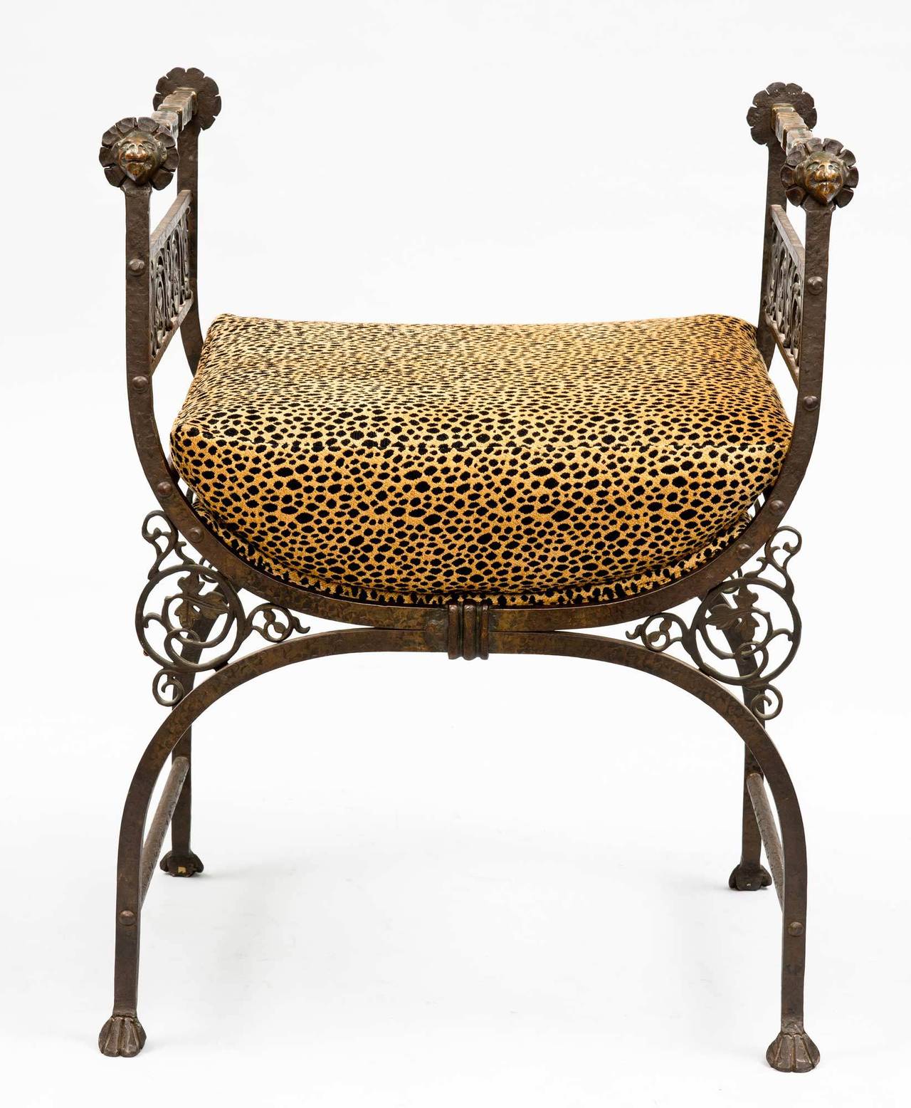 Bronze and wrought iron hall bench in Savonarola style on X-form bases with molded arms, lion’s head hand rests, pierced and scrolled foliate and grape decoration on the sides, padded seat upholstered in leopard patterned fabric, ending in stylized