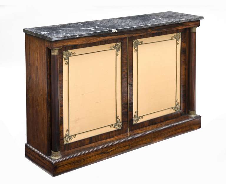 Fine quality rosewood side cabinet or credenza, the original grey marble top above a pair of paneled doors lined with gold silk held in place by an unusual gilt brass frame with shell motifs in the corners, flanked by two detached columns with gilt