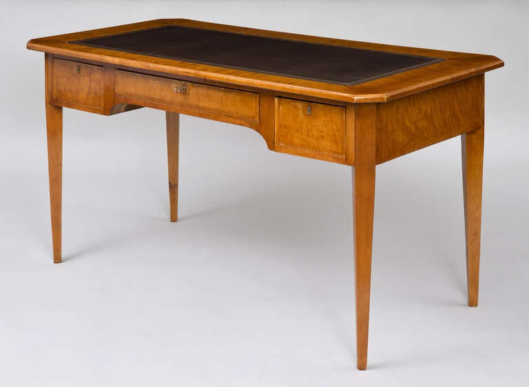 Elegant Swedish flame birch Neoclassical writing table in Biedermeier style with canted corners to top, frieze with three drawers, all with beech banding, dark brown leather writing surface with unusual vertical lined gilt-tooling, back is finished