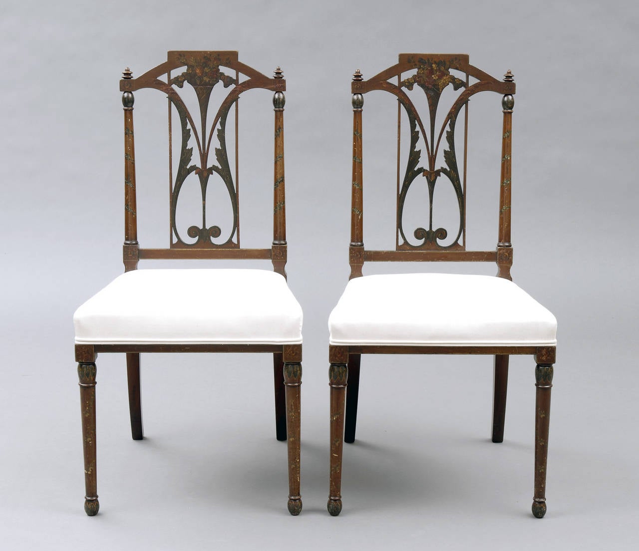 Pair of Edwardian painted side chairs with delicately shaped top rail and back splat decorated with bouquets of flowers and foliate designs.  The legs are turned and decorated with spirals of flower garlands.  The seat is upholstered in an off-white