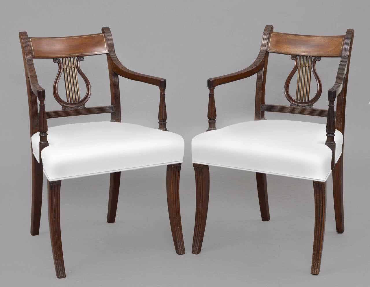 These mahogany armchairs have a top rail inlaid with brass, lyre-shaped splats inlaid with brass, a reeded frame, turned and reeded vase-shaped arm supports, sabre-shaped front and back legs and are upholstered in a white cotton fabric.

Item