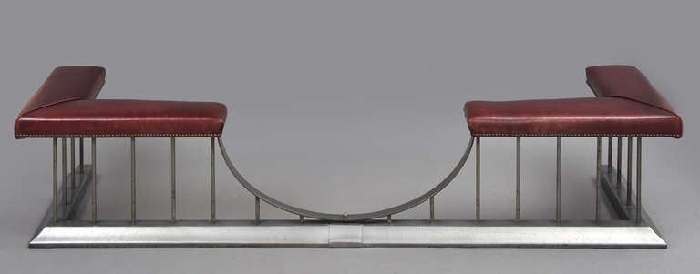 A club fender, the base in moulded steel. The burgundy-colored leather seat with brass tacks is supported by square upright steel rods with the front open in a half-circle for access to the fire. The inside measurements, inside the seat are 70? side