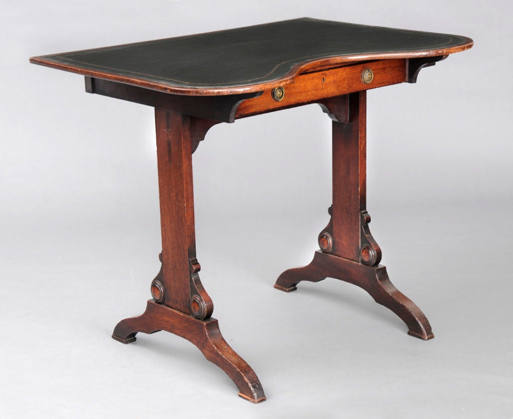 Regency mahogany kidney-shaped writing table with a single frieze drawer, opposing dummy drawer, pull-out pen drawer to the right side, raised on carved end supports on arched feet with high stretcher under drawer. Top with dark green gilt-tooled