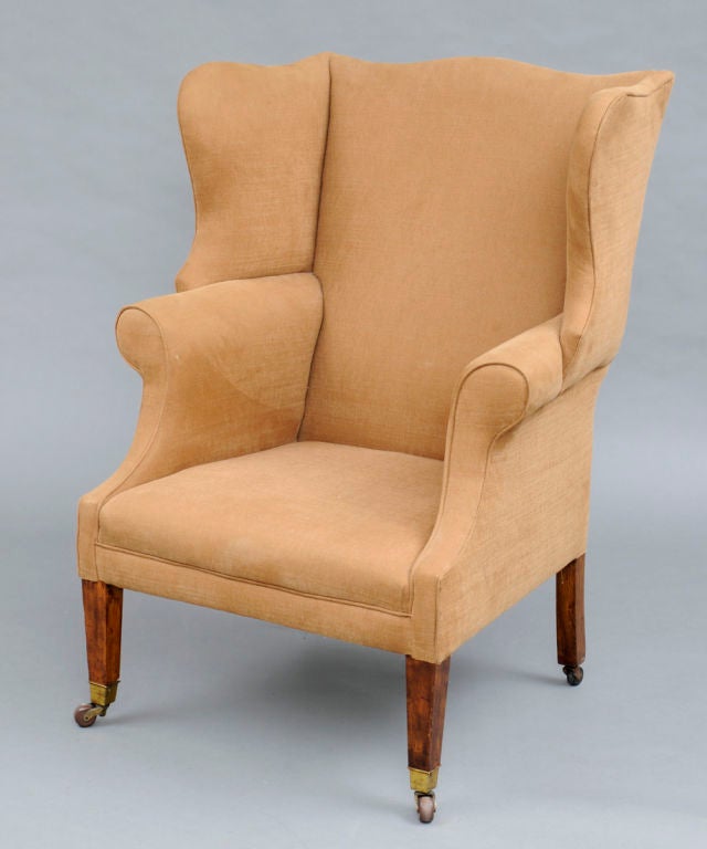 A late 19th century George III style mahogany wing chair, the curved crest above outward scrolling armrests, deep wings raised on square tapering legs on porcelain casters. It has an ash frame, mahogany front legs and ash back legs. Upholstered in