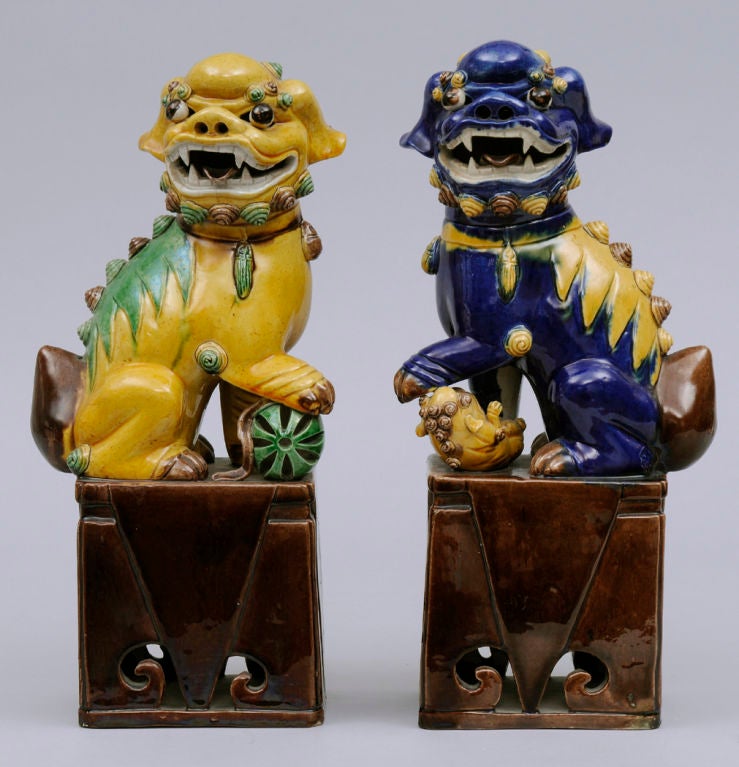 Pair of Chinese multi-colored models of Buddhistic lions or foo dogs, the male in yellow and green with his paw on a sphere, the female in cobalt blue and yellow holding her cub, mounted on brown pierced bases.