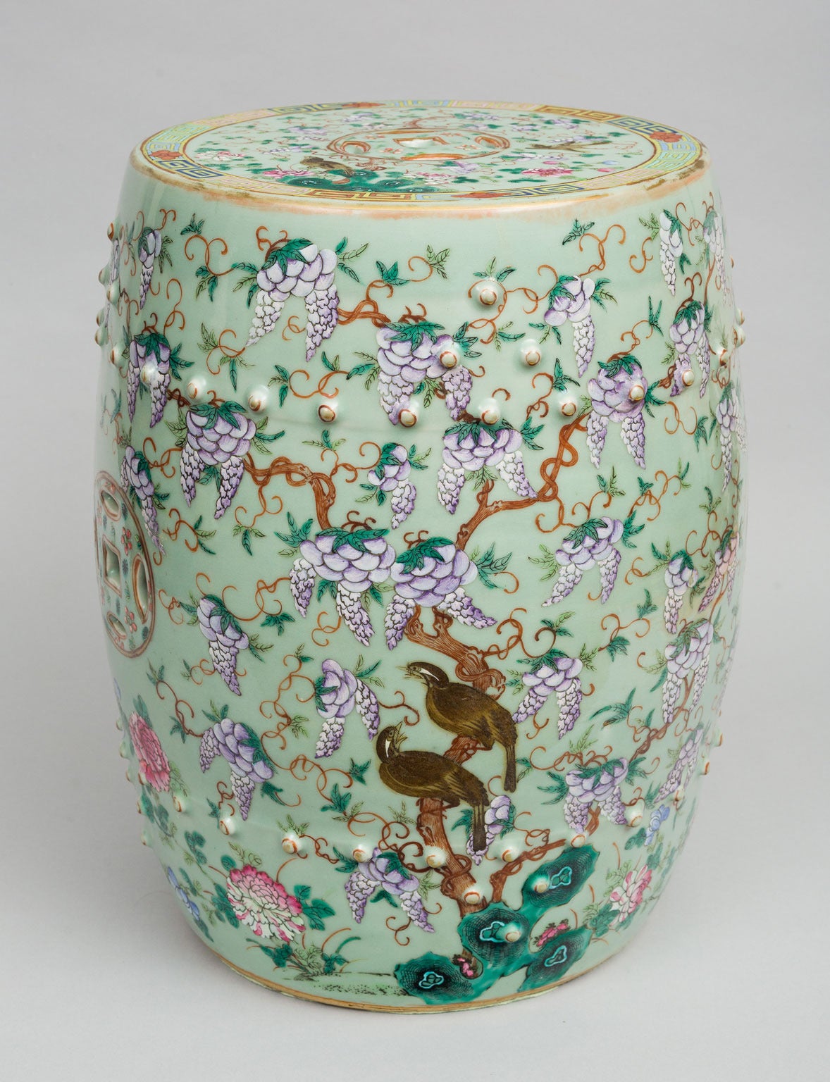 Exceptional Chinese porcelain barrel form garden seat decorated with hanging lavender wisteria blossoms and foliage, birds, chrysanthemums, pierced interlocking double-cash symbols on two sides and molded bands of studs on a celadon green