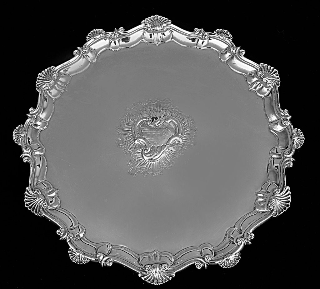 A George II sterling silver salver by Dorothy Sarbit of London with bold shell and C-scroll shaped border, the center with raised crest, on three scrolled feet.