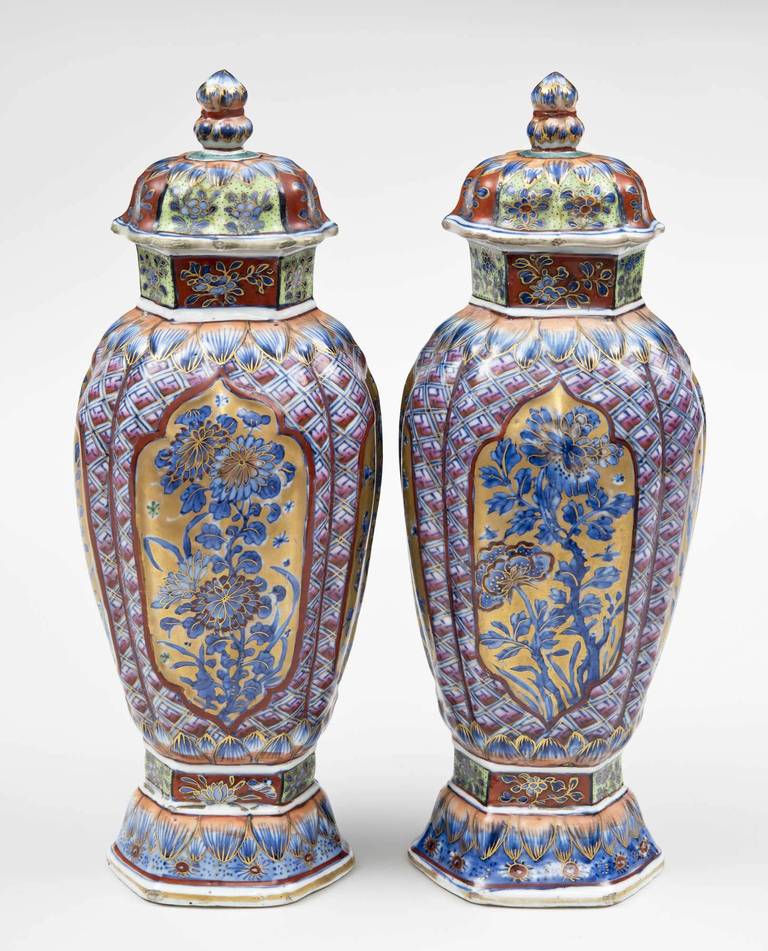 Pair of very finely decorated Chinese blue and white clobbered vases and lids. The neck and base are hexagonally shaped, the body is ribbed. Each of the four sides have shield shapes outlined in red within which are blue chrysanthemums on a gilded