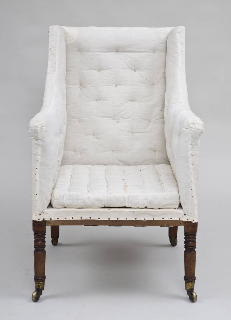 Regency library high-backed buttoned armchair with mahogany turned legs on casters, loose cushion, stripped to the original ticking.

    