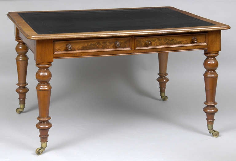 Early Victorian mahogany two-drawer writing table with black blind-tooled leather writing surface raised on turned legs ending in brass casters.  The drawers have wooden knobs.

 