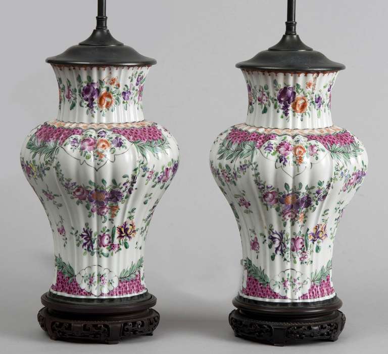 Pair of Samson porcelain baluster-shaped vase lamps on original antique Chinese pierced wooden stands. The body is ribbed and decorated in Famille Rose colors in the English Lowestoft style. 

Edmé Samson opened his ceramics firm Samson, Edmé et
