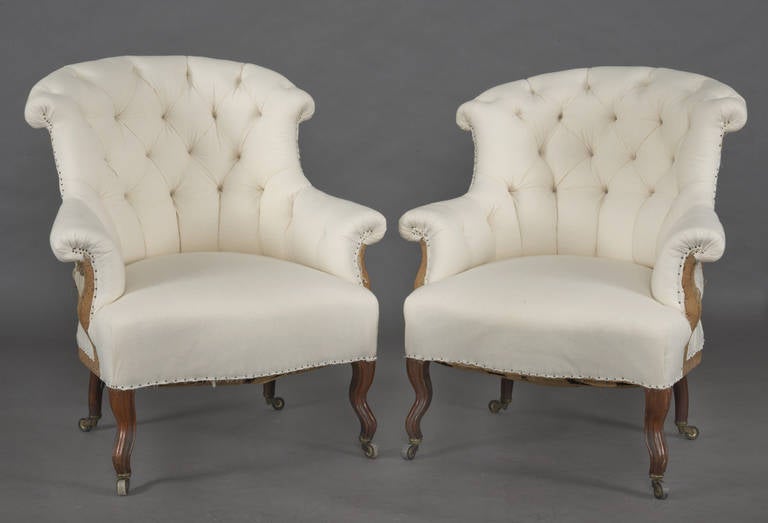 Pair of Napoleon III armchairs with curved and scrolled buttoned backs, rolled arms, serpentine shaped seat on mahogany shaped legs on casters and upholstered in white muslin.

 