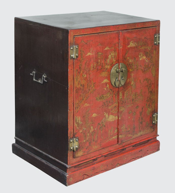 Period Chinese red (auspicious color of joy and happiness) lacquered cabinet with two doors, circular brass lock plates and hinges, decorated in gold leaf with hand painted river and mountain scenes. Iron carrying handles on the sides. Sides and top