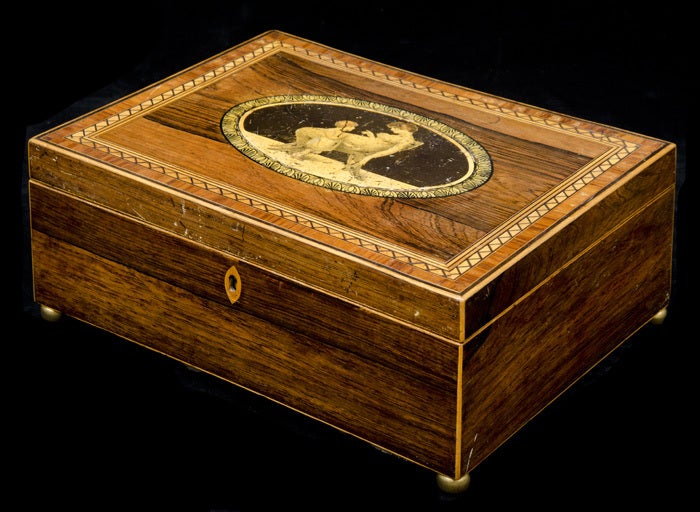 Regency rosewood box inlaid with rosewood, satinwood and ebonized stringing, the hinged top centered with a buck print of a mother sitting in a Klismos style chair attending her child, the oval gilded border with pen and ink drawing of egg and dart