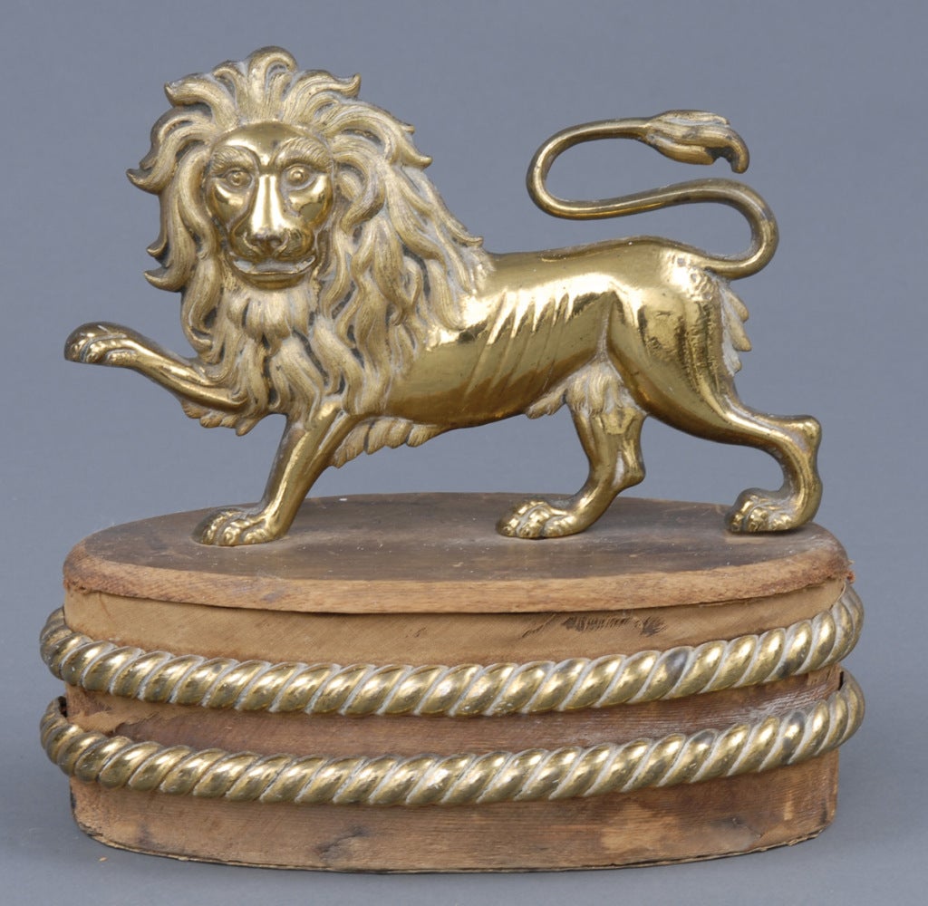 Wonderful gilded bronze lion ornament mounted on an oval pine block with two gilded bronze rope twists surrounding it. Remnants of the original red silk still remain. Originally affixed to the backs of the chairs in the House of Lords.