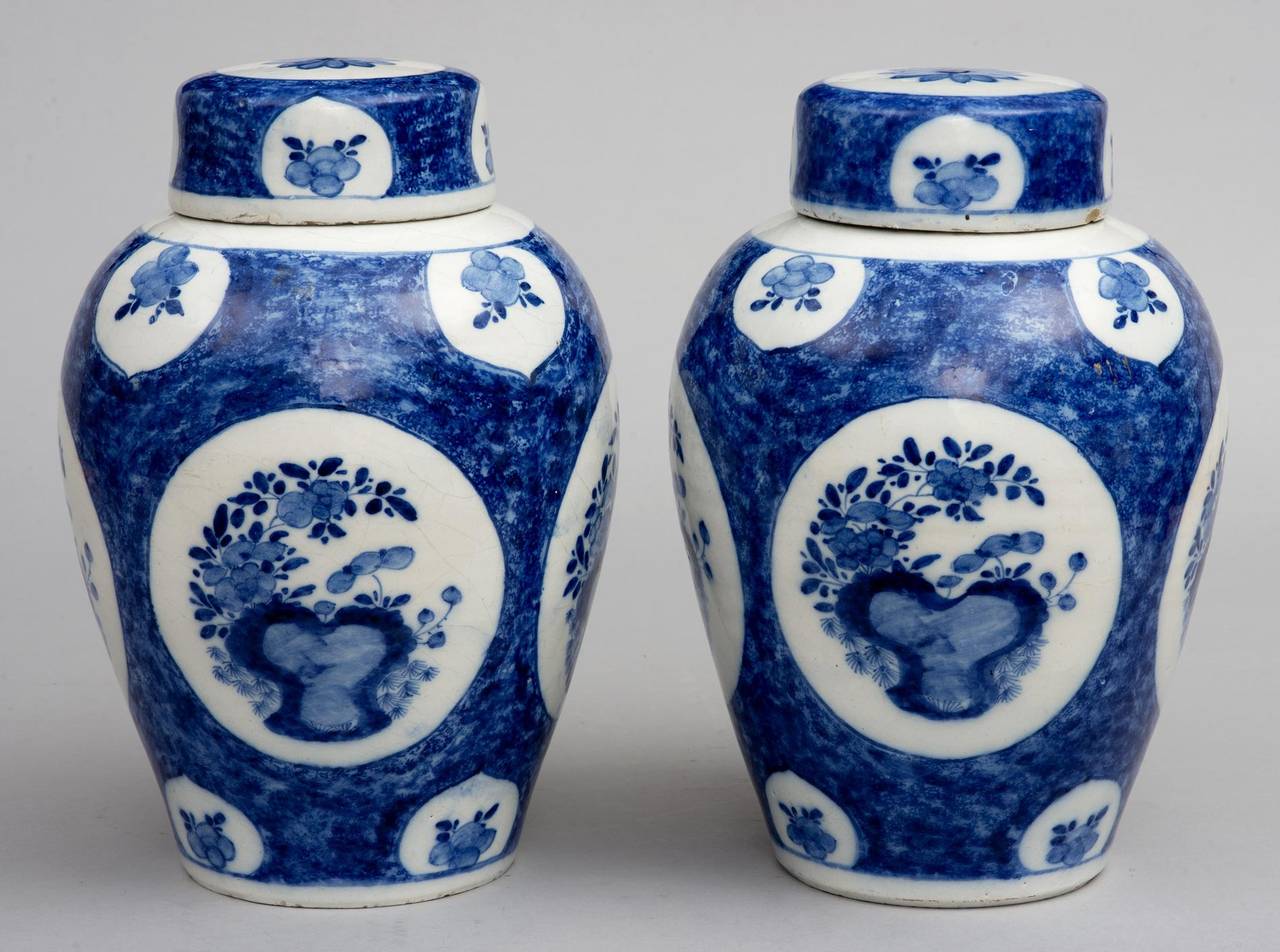 Pair of blue and white delft vases with lids in the Chinese taste, decorated with four large white roundels enclosing floral designs on a sponged background. The deep lids with stylized flowers.

        