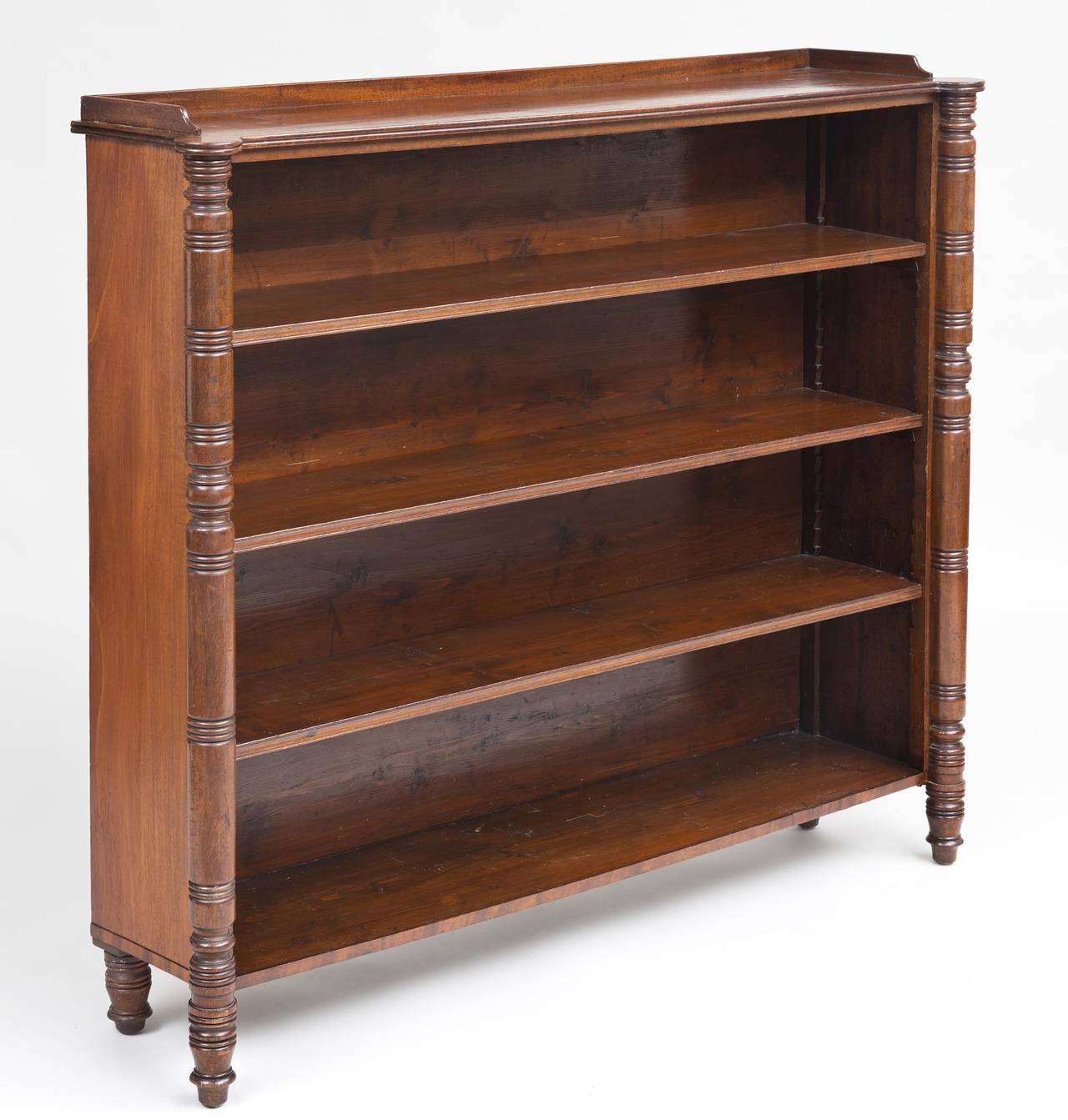 Regency mahogany open bookcase, the rectangular top with cookie-cutter corners and three-sided low gallery, above three adjustable shelves, turned column end supports on turned legs.

   