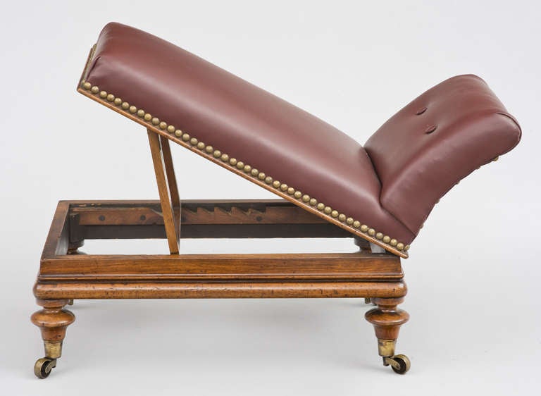 Mahogany gout stool that adjusts in height by a racheted stand, raised on turned legs and brass casters .  Upholstered in a burgundy-colored leather and brass tacks.