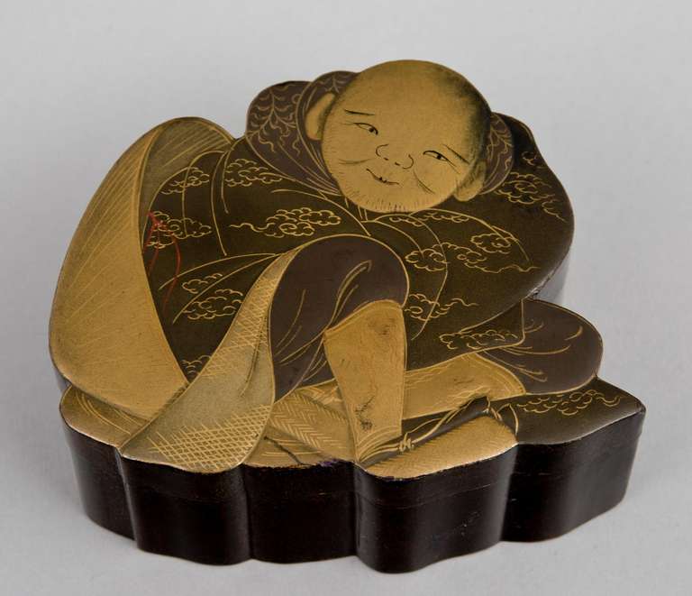 Japanese black and gilded lacquered box in the form of a small boy wrapped in silk robes, the bottom of the box and inside are speckled with tiny dots of iridescent orange.

 