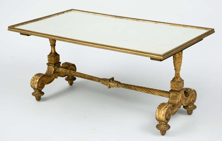 French giltwood coffee table with mirrored top, having carved end supports with acanthus leaf C-scrolls joined by spiral twist stretcher, raised on trumpet feet.  The base is 19th Century, the mirror is of later manufacture.

Item #7246