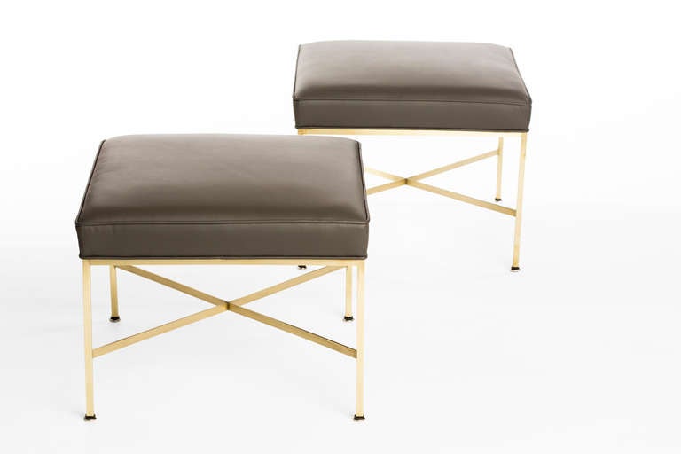 A pair of tailored, elegant Paul McCobb X-base stools with delicately proportioned frames of richly tinted unlacquered brass, newly upholstered in a luxurious elephant gray Spinneybeck leather.