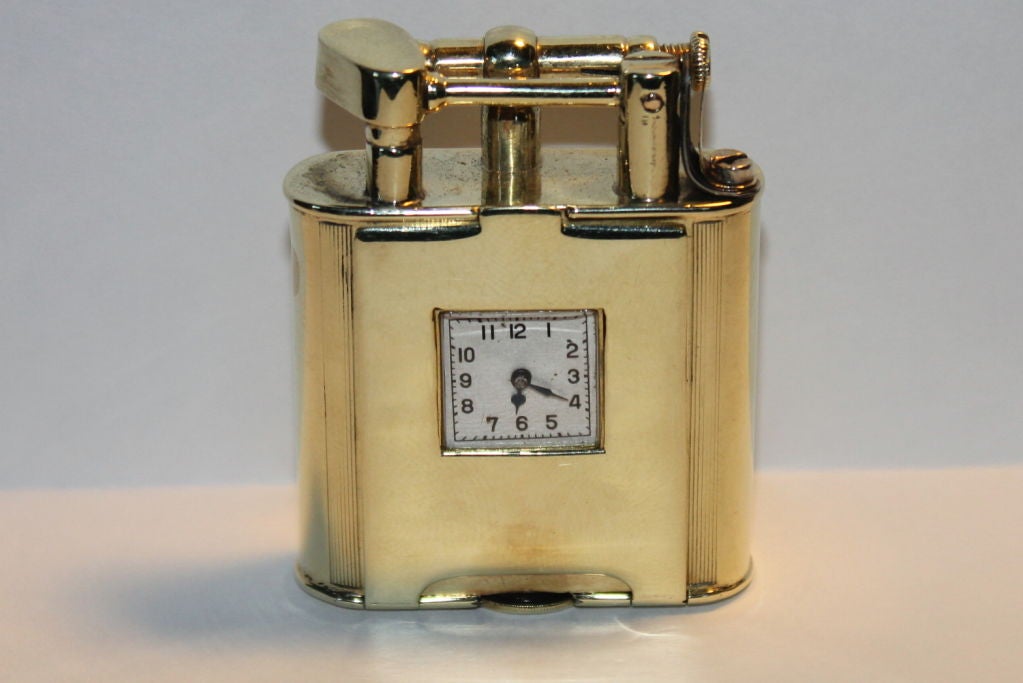 A really unusual 14k solid gold art deco swing arm lighter with a watch movement on the front. The lighter has it's original Dunhill slipcase. The watch is a mido movement and is running. Setting and winding it is accomplished by lifting the front