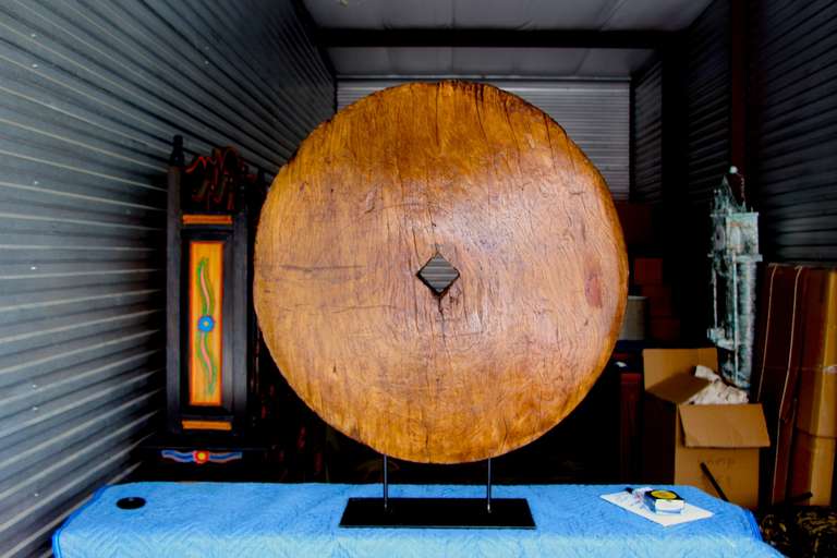 A large mounted Asian wooden wheel, at least 18th century in origin. It has been mounted on a stable iron base. One side which is facing forward in the 1st photograph is slightly concave.  A great decorative item.