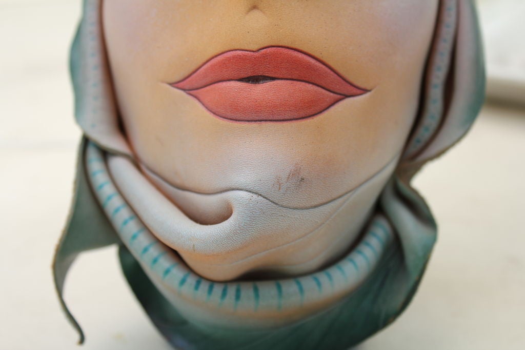 A most unusual piece of sculpture made out of leather and shaped and painted as a woman's face in hat. It is signed Gibson 1995 and Made in Canada.